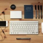Top view of a modern desk setup featuring electronics, stationery, and gadgets on a wooden surface.